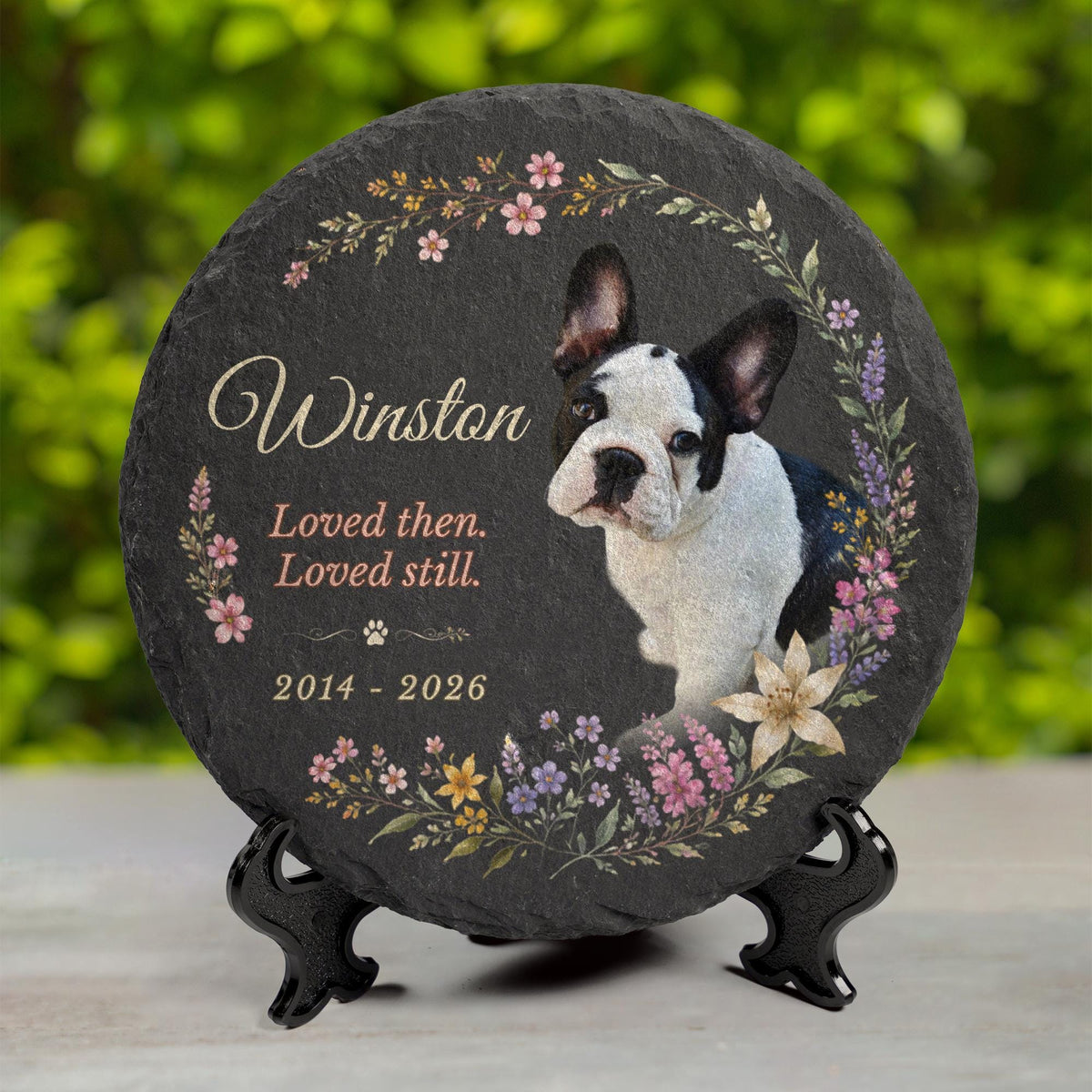 Personalized dog memorial stone displayed upright on an easel stand, showing the slate's chiseled edge and floral border.