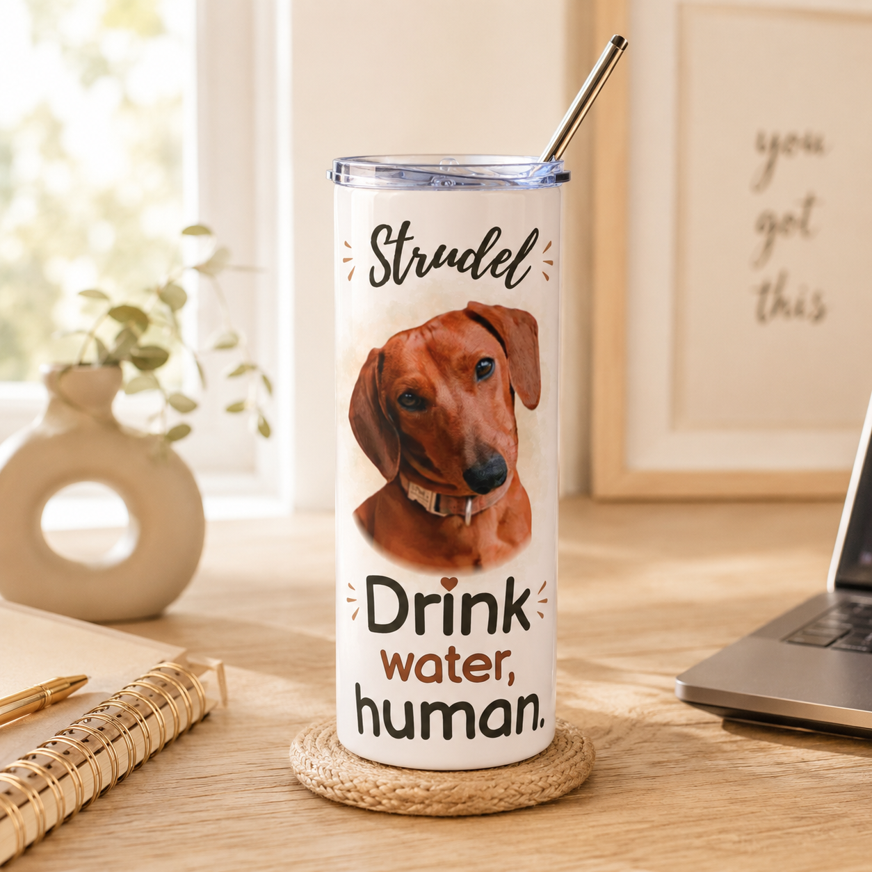 Dachshund-print dog mom tumbler resting on a coaster next to a notebook and laptop.