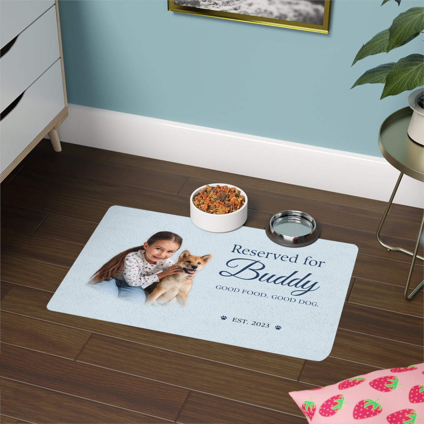 Blue dog placemat with an owner-and-dog photo on a dark wood floor beside a dresser and two bowls.
