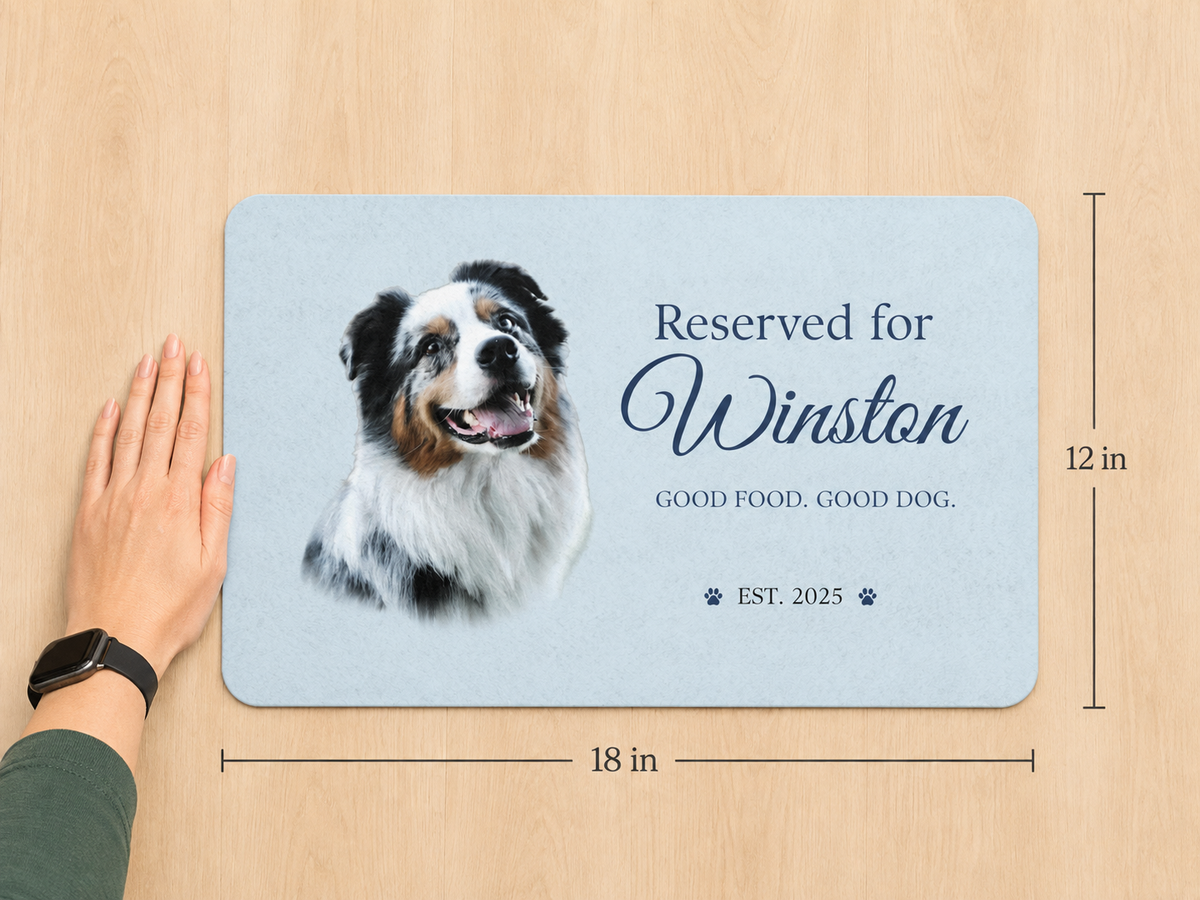 Hand beside the 12 x 18 inch personalized dog placemat, showing its size against a wood floor.