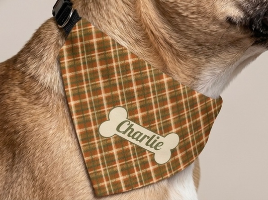 Close-up of a fawn dog wearing a rust and olive fall plaid dog bandana with the name Charlie on a cream bone-shaped patch.