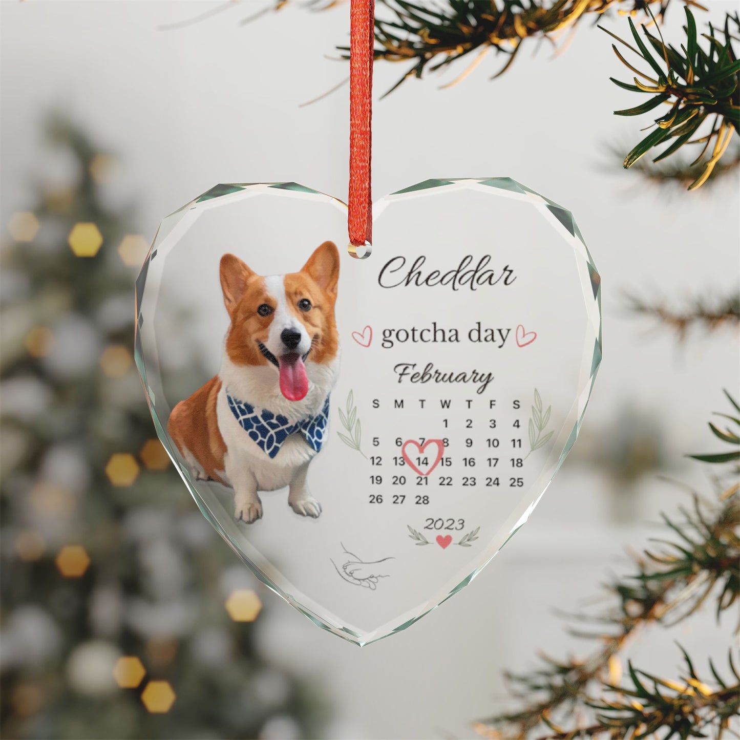 Personalized gotcha day dog ornament hanging in front of a lit Christmas tree, wide shot.