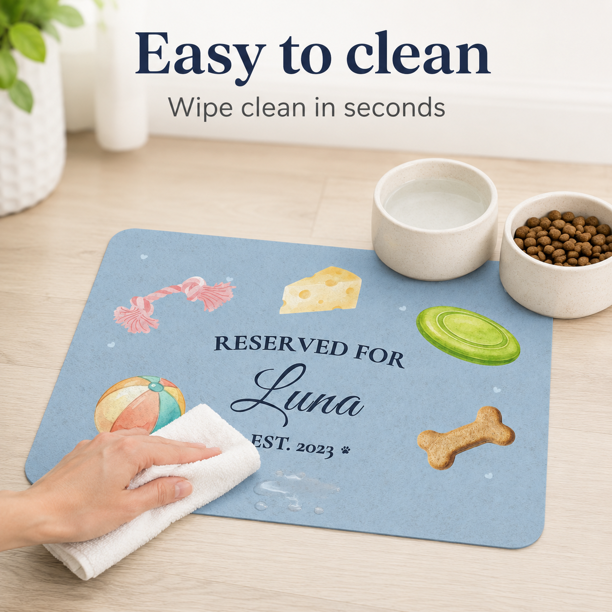 Hand wiping a blue personalized dog bowl mat clean with a damp cloth.
