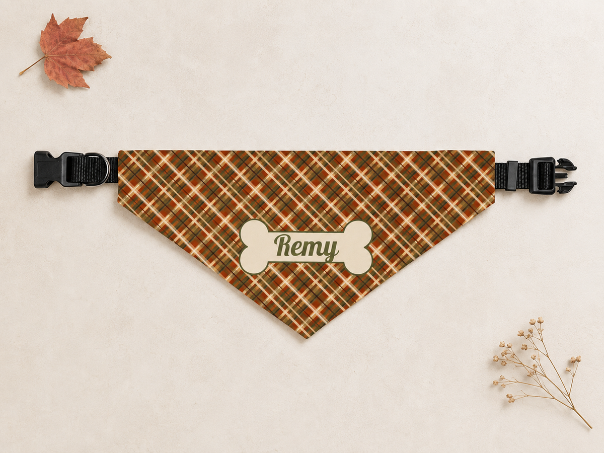 Fall plaid dog bandana laid flat with black clip buckles at both ends, name Remy on a bone patch, beside a maple leaf.