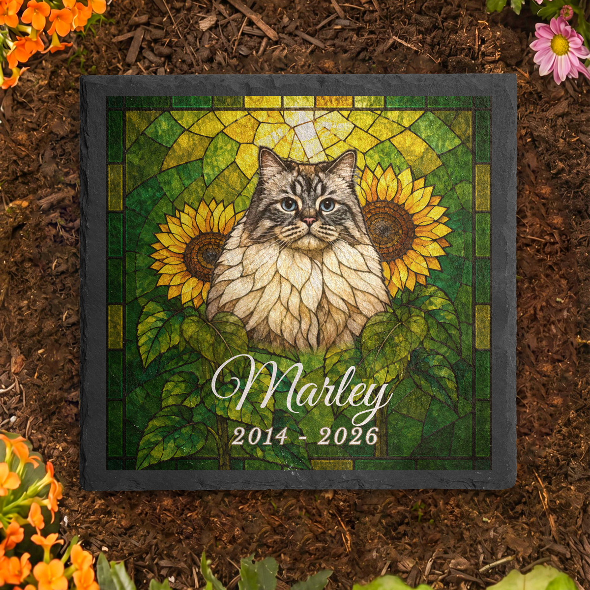 Stained glass cat memorial stone in a flower bed: grey tabby mosaic portrait with sunflowers and the name Marley.